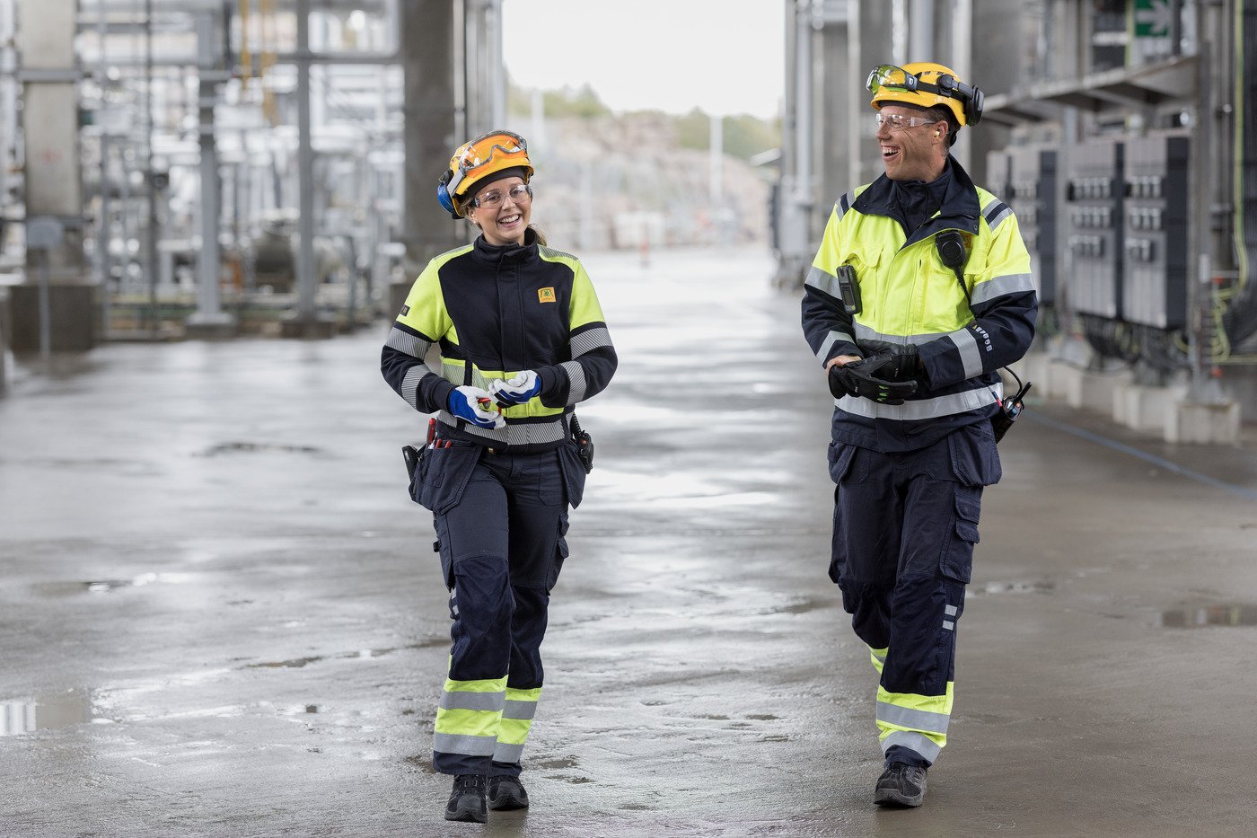 2 raffinaderiarbetare går genom raffinaderi, säkerhetsutrustning, man och kvinna